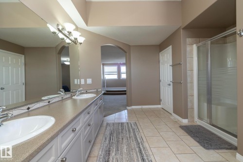 Bathroom featuring a stall shower, double vanity, light tile patterned floors, and suspended lighting - 16454 61A Street, Edmonton, AB - Indoor Photo Showing Bathroom
