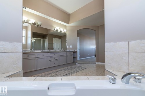 Full bathroom with tile walls, double vanity, light tile patterned floors, a stall shower, and a bath - 16454 61A Street, Edmonton, AB - Indoor Photo Showing Bathroom