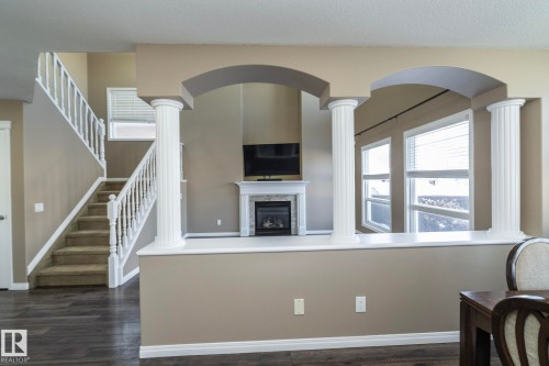 Living room featuring decorative columns, dark wood finished floors, a glass covered fireplace, and arched walkways - 16454 61A Street, Edmonton, AB - Indoor Photo Showing Other Room With Fireplace