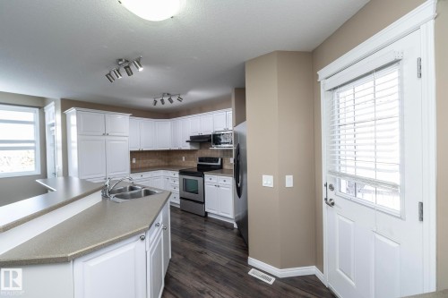 Kitchen with stainless steel appliances, white cabinetry, dark wood-style flooring, decorative backsplash, and a kitchen island with sink - 16454 61A Street, Edmonton, AB - Indoor Photo Showing Kitchen With Double Sink