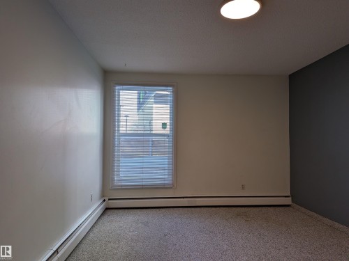 Carpeted spare room featuring a baseboard radiator and a textured ceiling - 109 7220 144 Avenue, Edmonton, AB - Indoor Photo Showing Other Room