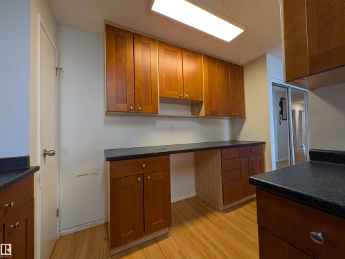 Kitchen with dark countertops, wood finish cabinetry, and light wood-type flooring - 109 7220 144 Avenue, Edmonton, AB - Indoor Photo Showing Other Room
