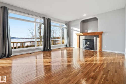 Unfurnished living room with light wood finished floors, a tiled fireplace, a water view, and recessed lighting - 12634 16A Avenue, Edmonton, AB - Indoor Photo Showing Living Room With Fireplace