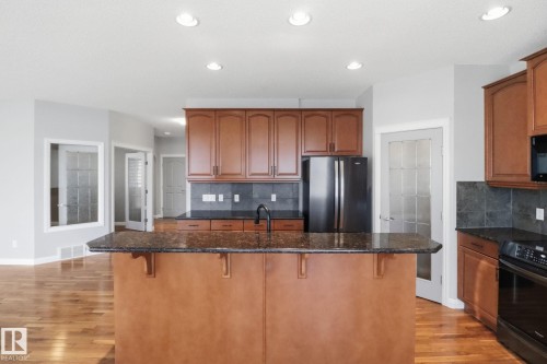 Kitchen with backsplash, dark stone counters, black appliances, a breakfast bar area, and light wood-style floors - 12634 16A Avenue, Edmonton, AB - Indoor Photo Showing Kitchen