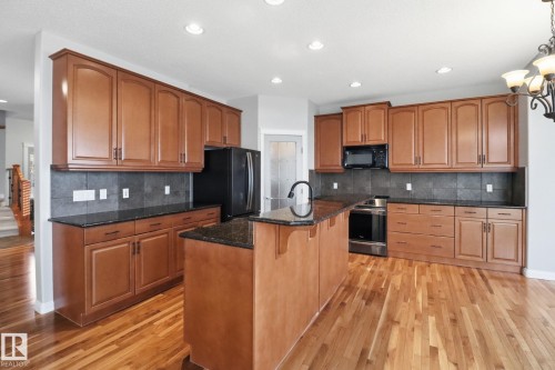 Kitchen featuring dark stone counters, a kitchen breakfast bar, black appliances, light wood-style flooring, and wood finish cabinets - 12634 16A Avenue, Edmonton, AB - Indoor Photo Showing Kitchen