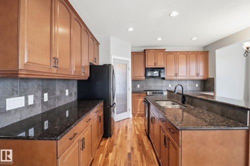 Kitchen with dark stone counters, light wood-style floors, wood finish cabinets, a kitchen island with sink, and recessed lighting - 12634 16A Avenue, Edmonton, AB - Indoor Photo Showing Kitchen With Double Sink