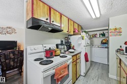 Kitchen featuring white appliances, washing machine and clothes dryer, a textured ceiling, light wood-style flooring, and wood finish cabinets - 