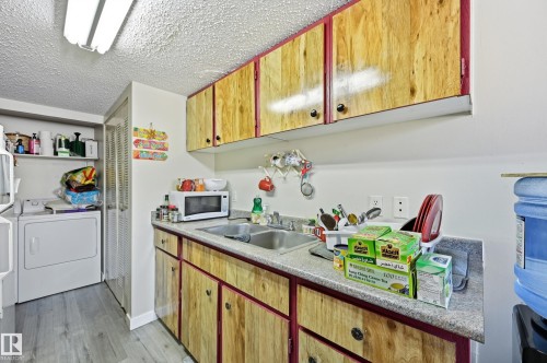 Kitchen with light countertops, a textured ceiling, white microwave, light wood finished floors, and washer and dryer - 1482 Lakewood Road W, Edmonton, AB - Indoor Photo Showing Laundry Room