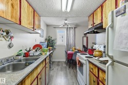 Kitchen with white appliances, a textured ceiling, wood finish cabinetry, ceiling fan, and light wood-style floors - 