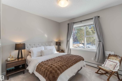 Carpeted bedroom featuring a textured ceiling and baseboard heating - 103 320 Ambleside Link Link Sw, Edmonton, AB - Indoor Photo Showing Bedroom
