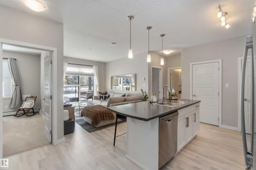 Kitchen featuring open floor plan, white cabinetry, dark countertops, stainless steel appliances, and an island with sink - 103 320 Ambleside Link Link Sw, Edmonton, AB - Indoor Photo Showing Kitchen With Upgraded Kitchen