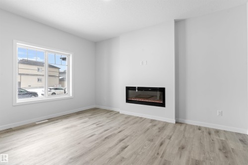 Unfurnished living room with a glass covered fireplace, light wood finished floors, and a textured ceiling - 320 Munn Way, Leduc, AB - Indoor Photo Showing Other Room With Fireplace