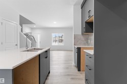 Two tone kitchen featuring dual tone cabinets, light wood-style floors, light stone countertops, tasteful backsplash, and a kitchen island with sink - 