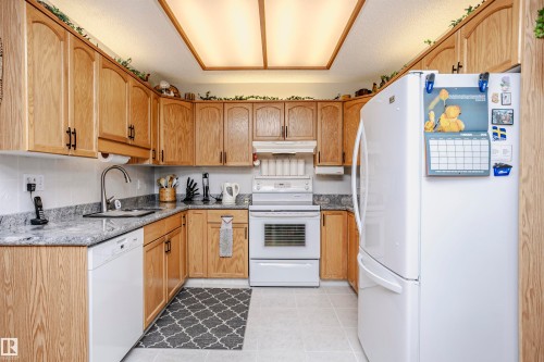 Kitchen featuring white appliances, dark stone counters, light tile patterned flooring, and a textured ceiling - 408 10935 21 Avenue, Edmonton, AB - Indoor Photo Showing Kitchen