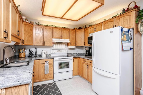 Kitchen featuring white appliances, light stone countertops, light tile patterned flooring, and a textured ceiling - 408 10935 21 Avenue, Edmonton, AB - Indoor Photo Showing Kitchen