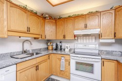 Kitchen featuring white appliances, light stone counters, light wood finish cabinets, and a textured ceiling - 