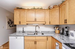 Kitchen with light wood finish cabinetry, dishwasher, light stone countertops, wood finished floors, and a textured ceiling - 