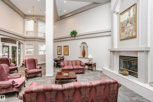 Living area with a tiled fireplace, a high ceiling, ceiling fan, baseboard heating, and carpet floors - 408 10935 21 Avenue, Edmonton, AB - Indoor Photo Showing Living Room With Fireplace