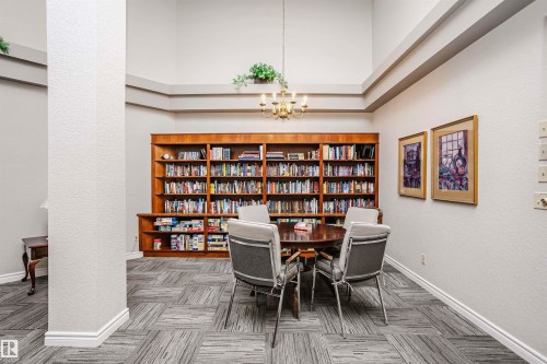 Office featuring hanging lights, carpet flooring, a textured wall, wall of books, and a high ceiling - 408 10935 21 Avenue, Edmonton, AB - Indoor Photo Showing Other Room
