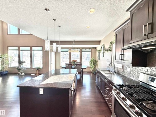 Kitchen featuring stainless steel gas stove, dark stone counters, hanging light fixtures, dark wood finish cabinetry, and a textured ceiling - 1019 174 Street, Edmonton, AB - Indoor Photo Showing Kitchen With Double Sink With Upgraded Kitchen