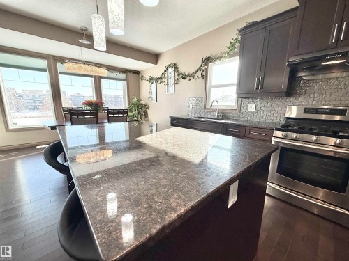 Kitchen featuring gas stove, dark wood finished floors, dark stone countertops, a kitchen island, and backsplash - 1019 174 Street, Edmonton, AB - Indoor Photo Showing Kitchen With Upgraded Kitchen