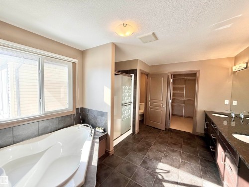 Bathroom with double vanity, a spacious closet, a garden tub, a textured ceiling, and dark tile patterned floors - 1019 174 Street, Edmonton, AB - Indoor Photo Showing Bathroom
