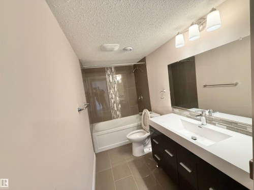 Full bath with vanity, shower / tub combo with curtain, a textured ceiling, and dark tile patterned floors - 1019 174 Street, Edmonton, AB - Indoor Photo Showing Bathroom