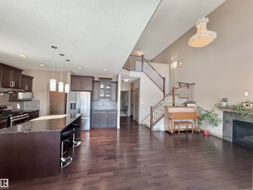 Kitchen with dark stone countertops, dark wood finish cabinets, a breakfast bar, stainless steel appliances, and a textured ceiling - 1019 174 Street, Edmonton, AB - Indoor Photo Showing Kitchen With Stainless Steel Kitchen With Upgraded Kitchen