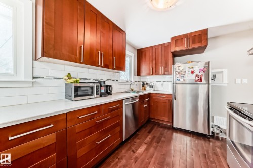 Kitchen featuring stainless steel appliances, backsplash, dark wood finished floors, wood finish cabinetry, and light stone counters - 12332 129 Street, Edmonton, AB - Indoor Photo Showing Kitchen With Double Sink