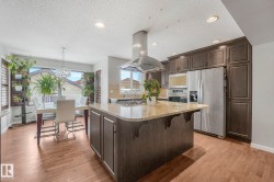 Kitchen with dark wood finish cabinets, light stone countertops, stainless steel appliances, a center island, and island exhaust hood - 