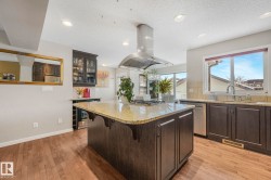 Kitchen with dark wood finish cabinets, a kitchen island, light stone countertops, a breakfast bar area, and recessed lighting - 