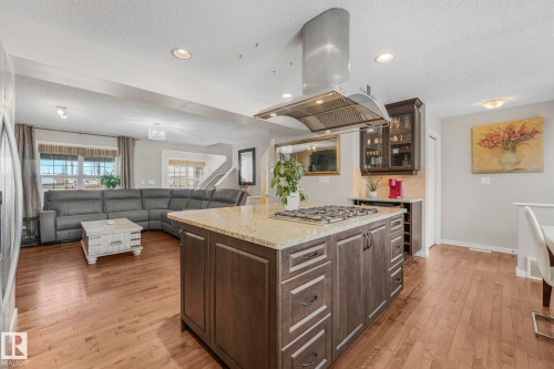 Kitchen featuring dark wood finish cabinetry, light stone countertops, island range hood, glass insert cabinets, and open floor plan - 281 Southwick Way, Leduc, AB - Indoor Photo Showing Kitchen