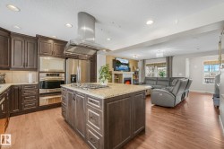 Kitchen featuring dark wood finish cabinetry, island exhaust hood, light stone countertops, light wood-type flooring, and recessed lighting - 