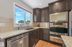 Kitchen with dark wood finish cabinetry, stainless steel appliances, light stone countertops, a warming drawer, and light wood-style flooring - 