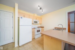 Kitchen with white appliances, a peninsula, a kitchen bar, light wood finish cabinets, and light countertops - 
