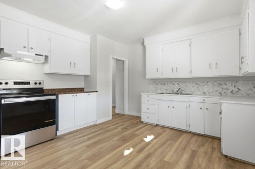 Kitchen with stainless steel range with electric stovetop, white cabinetry, light wood-type flooring, and backsplash - 10704 96 St Nw, Edmonton, AB - Indoor Photo Showing Kitchen