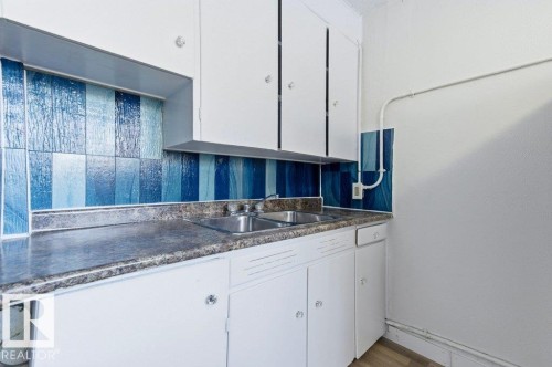 Kitchen with white cabinets, dark countertops, and light wood-style flooring - 10704 96 St Nw, Edmonton, AB - Indoor Photo Showing Kitchen With Double Sink