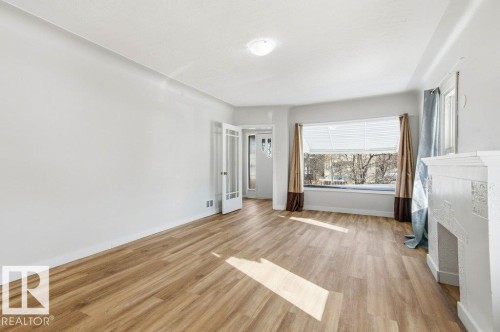 Unfurnished bedroom featuring light wood-style floors and a fireplace - 10704 96 St Nw, Edmonton, AB - Indoor With Fireplace