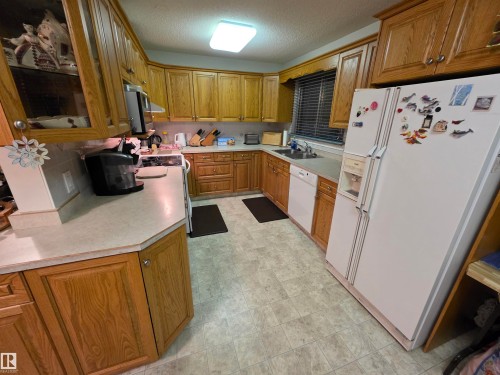 Kitchen featuring white appliances, light countertops, wood finish cabinetry, glass fronted cabinets, and a textured ceiling - 4400 45 Avenue, Stony Plain, AB - Indoor Photo Showing Kitchen