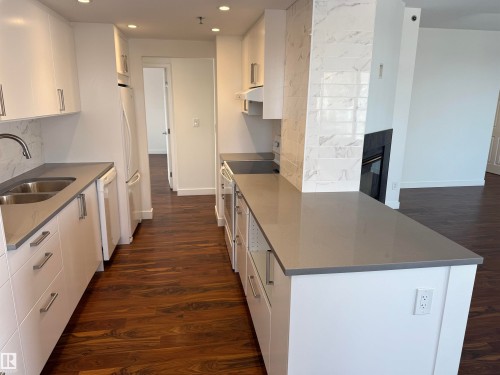 Kitchen featuring dark wood-style flooring, decorative backsplash, dark stone countertops, white cabinets, and white appliances - 605 8728 Gateway Boulevard, Edmonton, AB - Indoor Photo Showing Kitchen With Double Sink