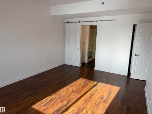 Unfurnished bedroom featuring dark wood finished floors, a barn door, and ensuite bath - 605 8728 Gateway Boulevard, Edmonton, AB - Indoor Photo Showing Other Room