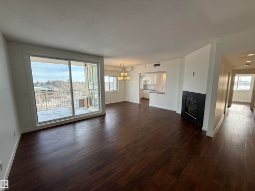 Unfurnished living room with suspended lighting, dark wood-type flooring, a fireplace, and a textured ceiling - 605 8728 Gateway Boulevard, Edmonton, AB - Indoor Photo Showing Living Room