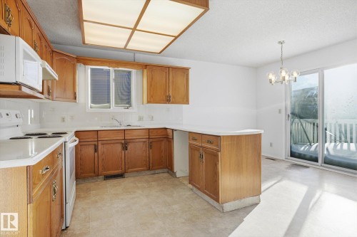 Kitchen featuring white appliances, a peninsula, wood finish cabinetry, light countertops, and a chandelier - 17816 94 Street, Edmonton, AB - Indoor Photo Showing Kitchen