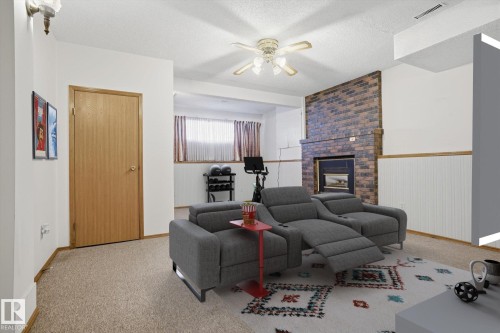 Carpeted living room with a ceiling fan, a fireplace, a textured ceiling, and a wainscoted wall - 17816 94 Street, Edmonton, AB - Indoor Photo Showing Living Room With Fireplace