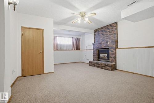 Unfurnished living room featuring ceiling fan, a textured ceiling, carpet flooring, a fireplace, and wainscoting - 17816 94 Street, Edmonton, AB - Indoor With Fireplace