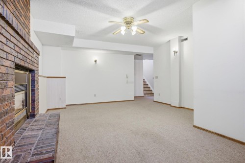Unfurnished living room featuring a brick fireplace, ceiling fan, light carpet, and a textured ceiling - 17816 94 Street, Edmonton, AB - Indoor Photo Showing Other Room