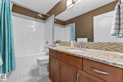 Full bath with vanity, shower / bath combination with curtain, backsplash, a textured ceiling, and light tile patterned floors - 2036 Hilliard Place, Edmonton, AB - Indoor Photo Showing Bathroom