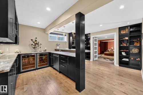 Indoor wet bar with dark cabinets, pendant lighting, light wood-style flooring, and light stone countertops - 2036 Hilliard Place, Edmonton, AB - Indoor Photo Showing Kitchen With Upgraded Kitchen