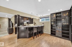 Kitchen with glass insert cabinets, dark wood finish cabinetry, a kitchen breakfast bar, pendant lighting, and light wood-style flooring - 