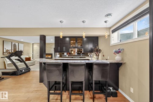 Bar area featuring decorative light fixtures, glass fronted cabinets, light wood-type flooring, light stone countertops, and a textured ceiling - 2036 Hilliard Place, Edmonton, AB - Indoor